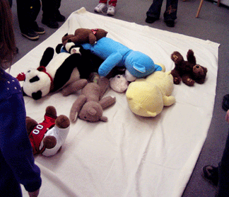 Children bouncing teddy bears on a blanket